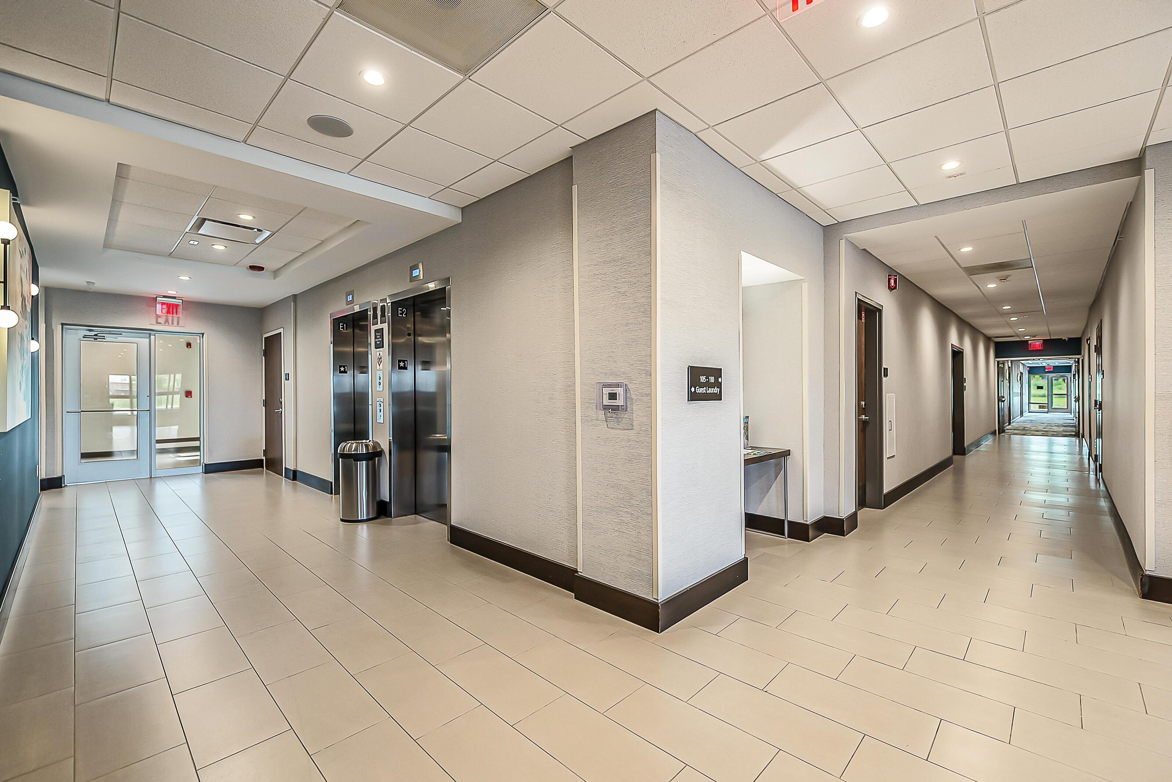 A clean, modern hallway with an elevator, a trash bin, and a sign indicating the exit.