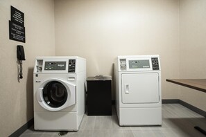 A laundry area with two front-loading washers and dryers, a recycling bin, and a phone for emergency assistance. - Hampton Inn & Suites Howell (Howell)