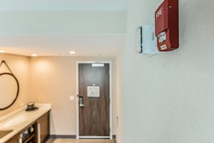 Un pasillo con una puerta de madera, un detector de incendios y un lavamanos.
