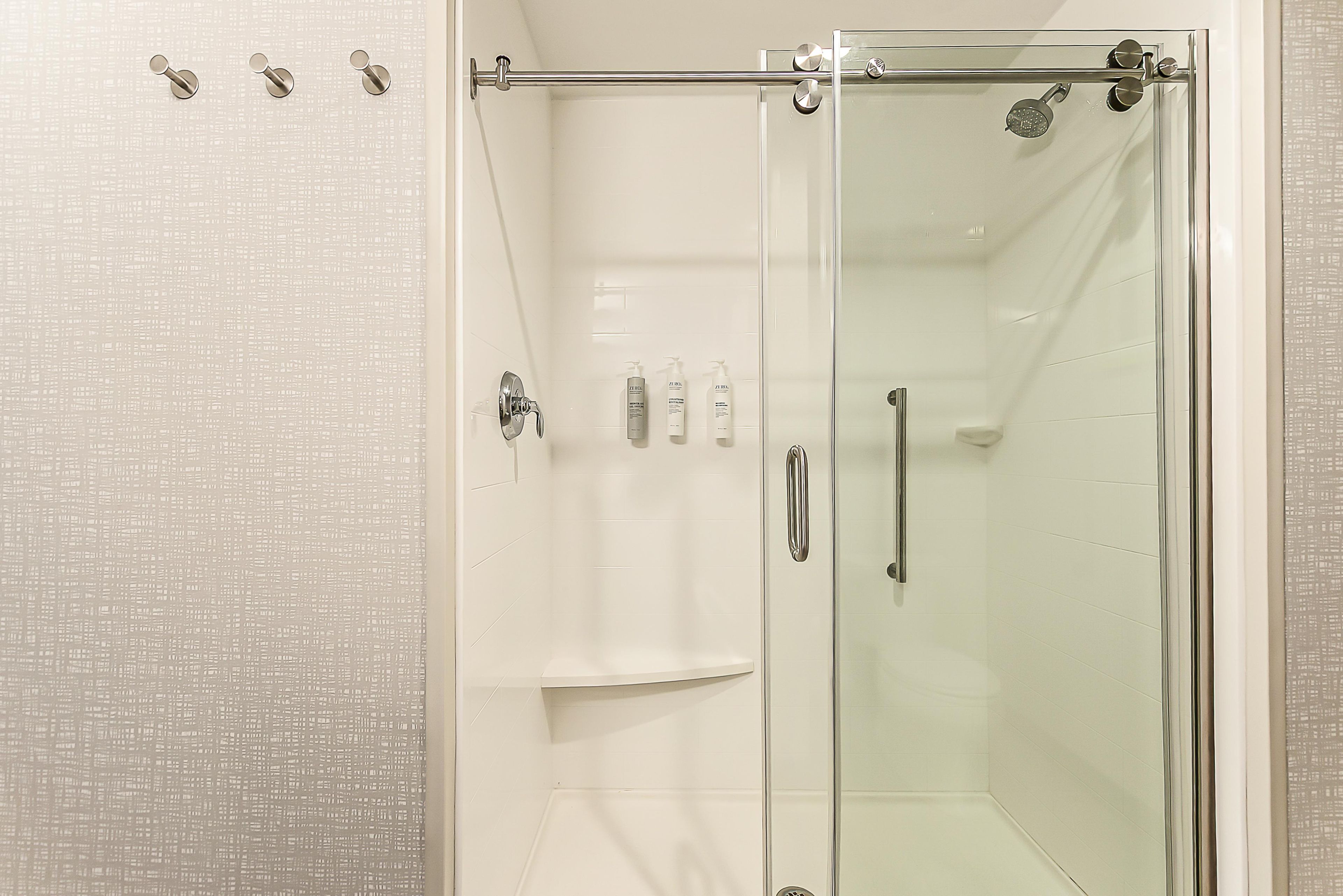 A glass-enclosed shower stall with a handheld showerhead, a glass door, and a towel rack.