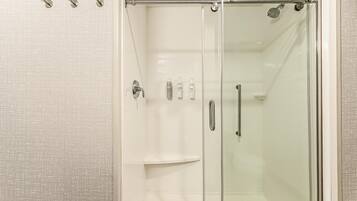A glass-enclosed shower stall with a handheld showerhead, a glass door, and a towel rack.