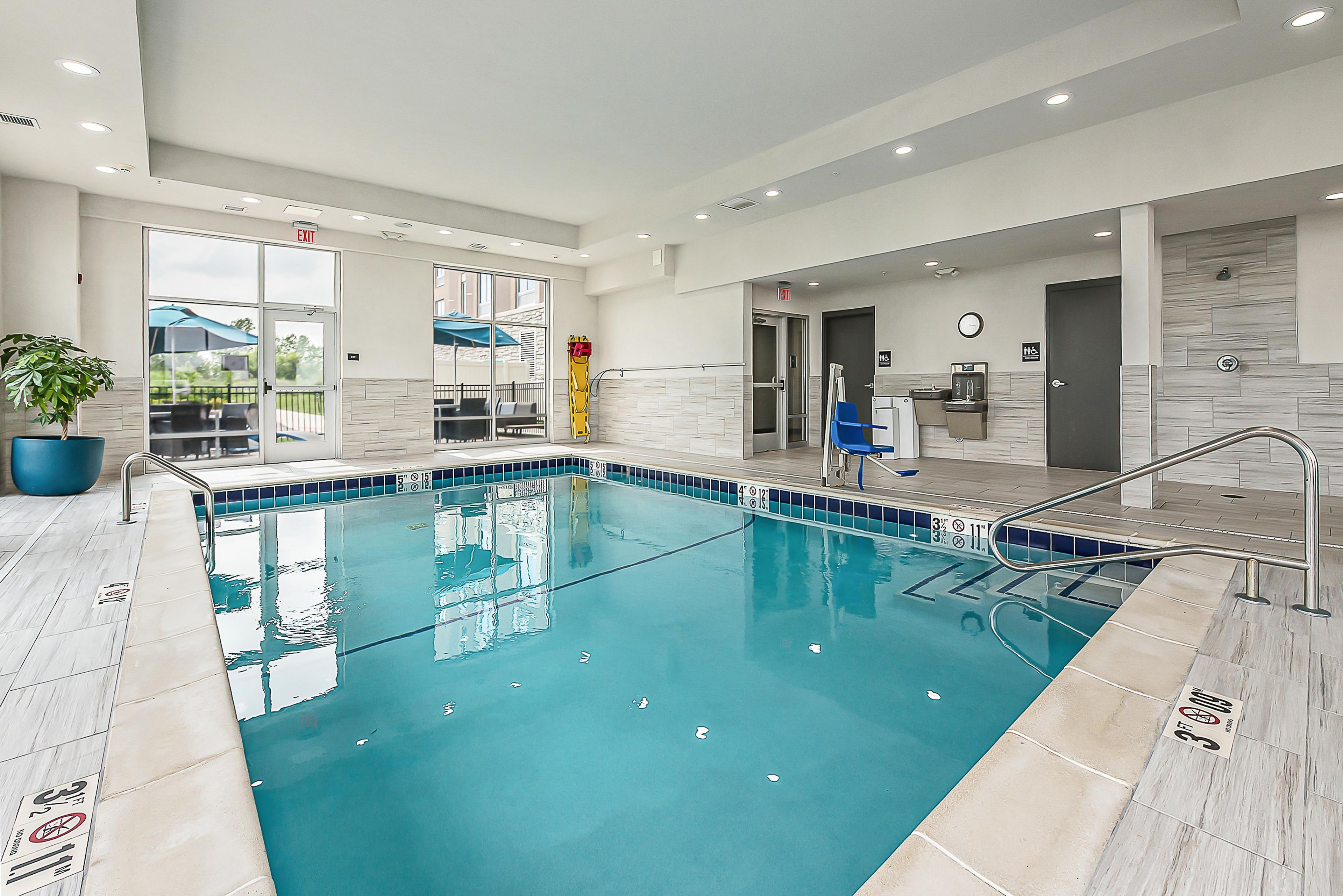 Une piscine intérieure moderne, dotée d’une eau claire, d’un bord carrelé et d’une échelle en métal.