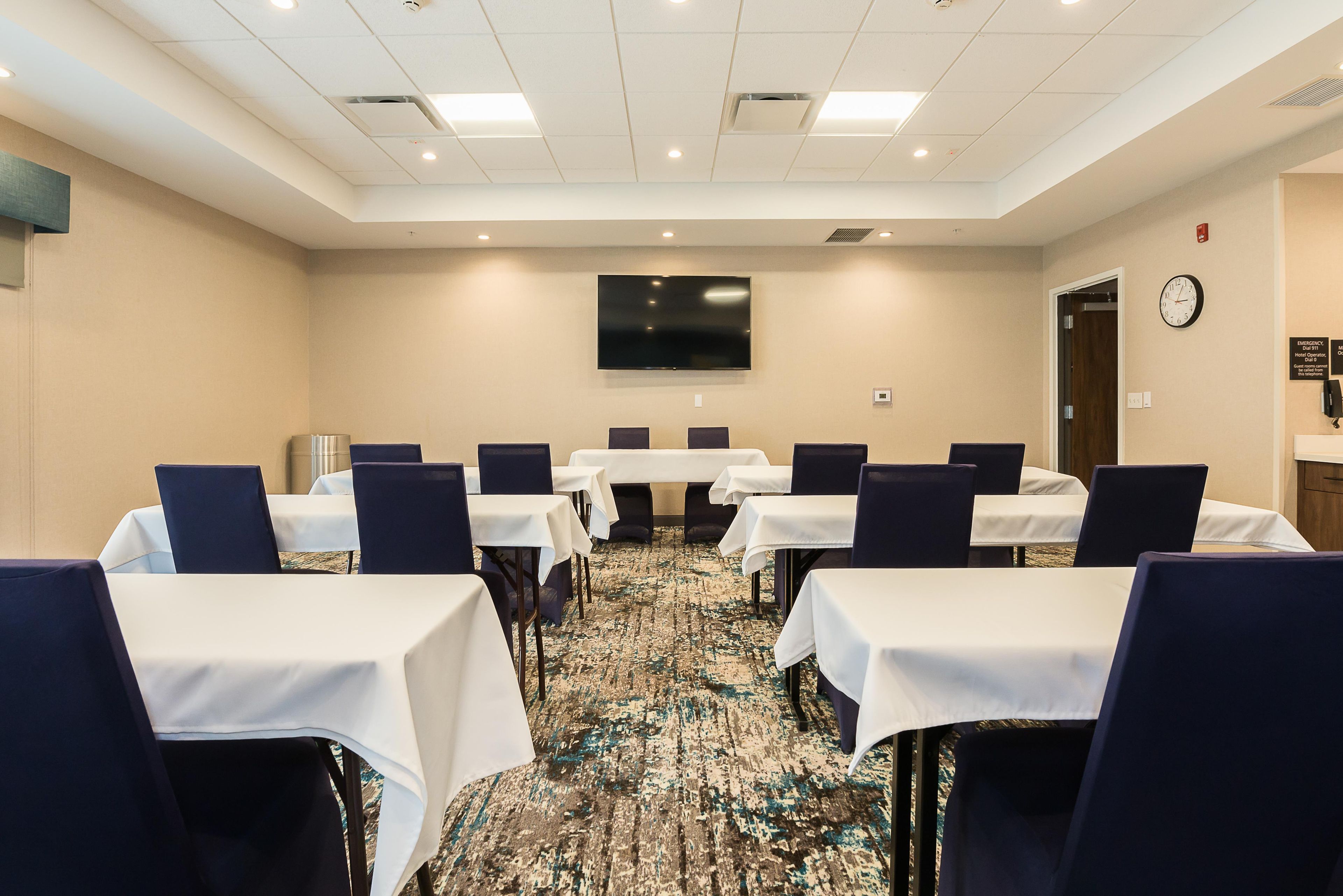 A conference room with tables and chairs, a flat-screen TV on the wall, and a clock on the wall.