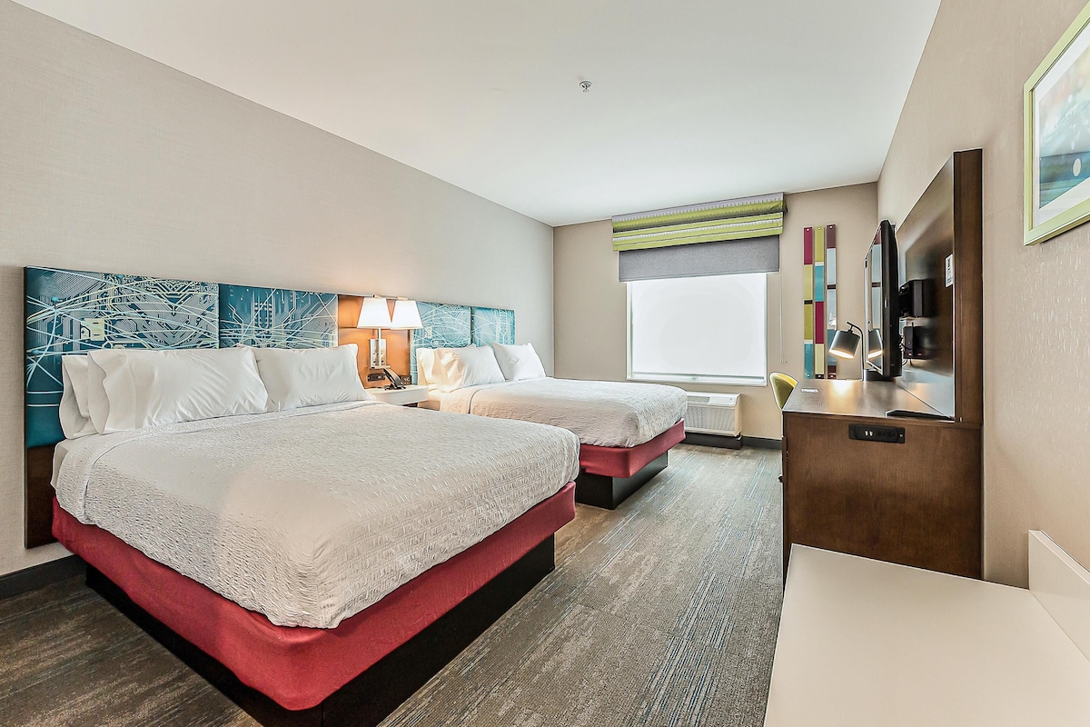Habitación de hotel con dos camas, un escritorio, una silla, un televisor y una ventana con vistas.