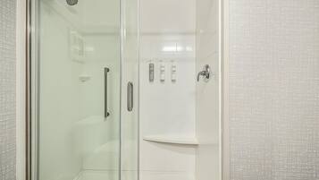 A glass-enclosed shower stall with a glass door, a showerhead, and a shelf with toiletries.