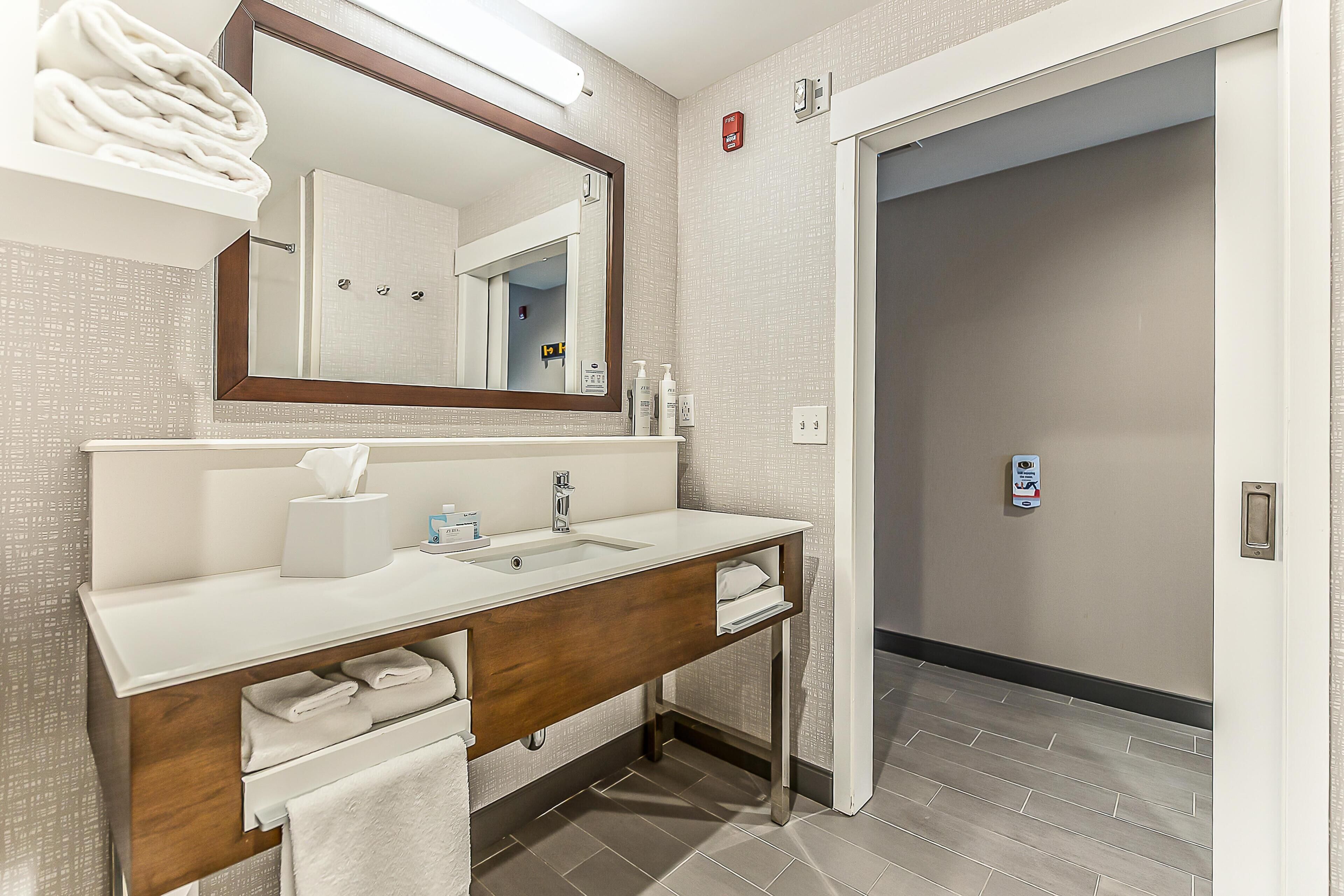 A modern bathroom with a white sink, wooden vanity, and a large mirror.