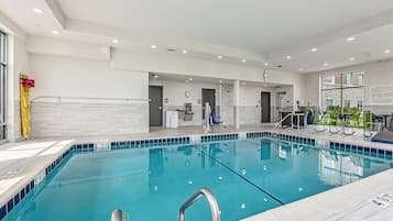 Una piscina interior moderna con marcas de carriles bien definidas, una silla de socorrista y una zona de recepción con un reloj y carteles informativos.