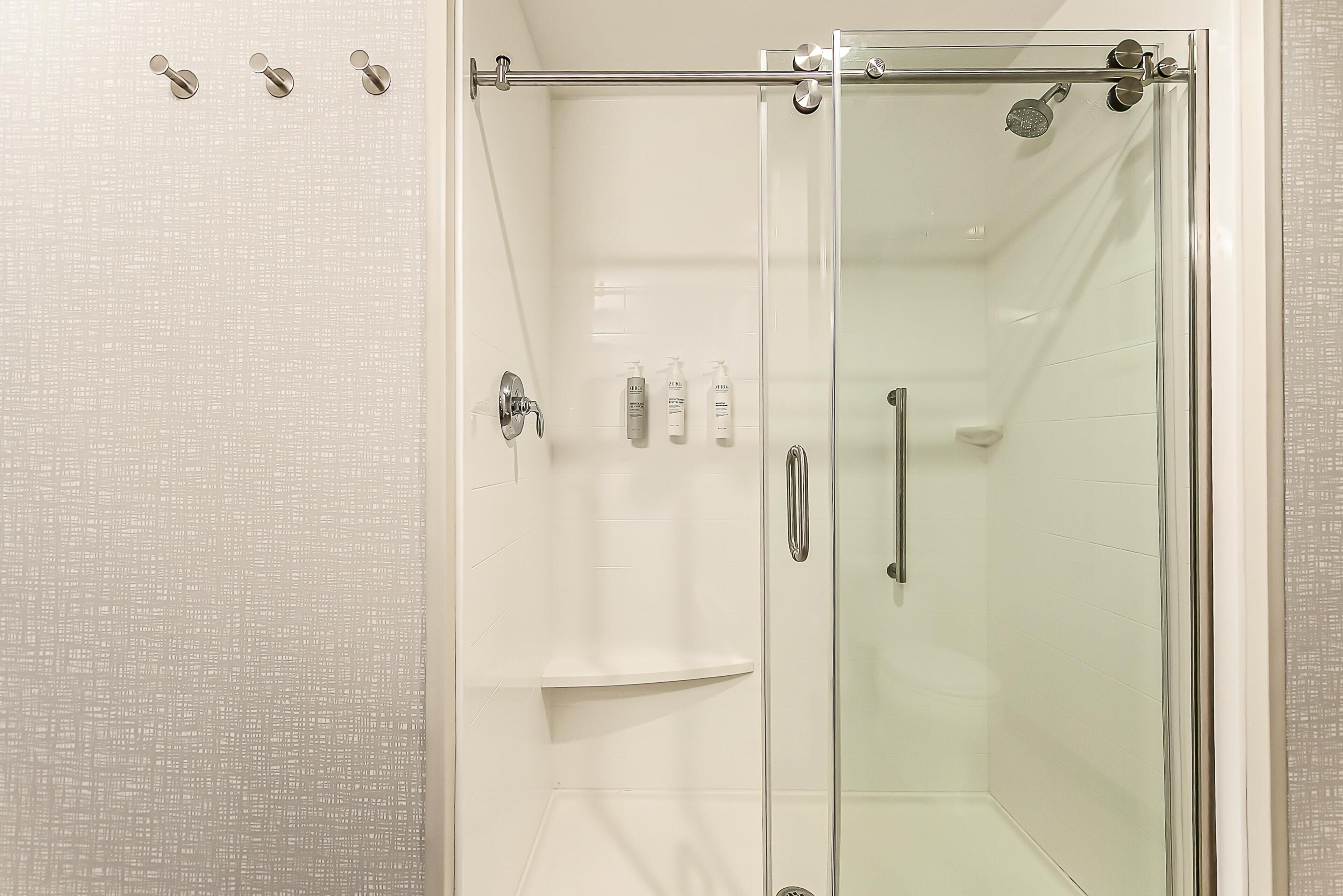 A glass-enclosed shower stall with a handheld showerhead, a glass door, and a towel rack.
