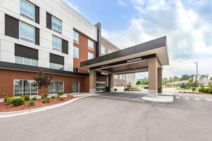 A modern building with a 'welcome' sign, large windows, and a landscaped entrance area.