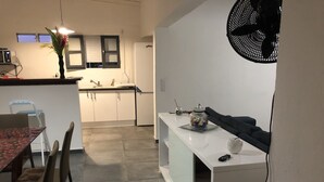 Eine moderne Küche mit weißen Schränken, ein Essbereich mit einem roten Tisch und Stühlen sowie eine kleine Kücheninsel mit Ventilator.