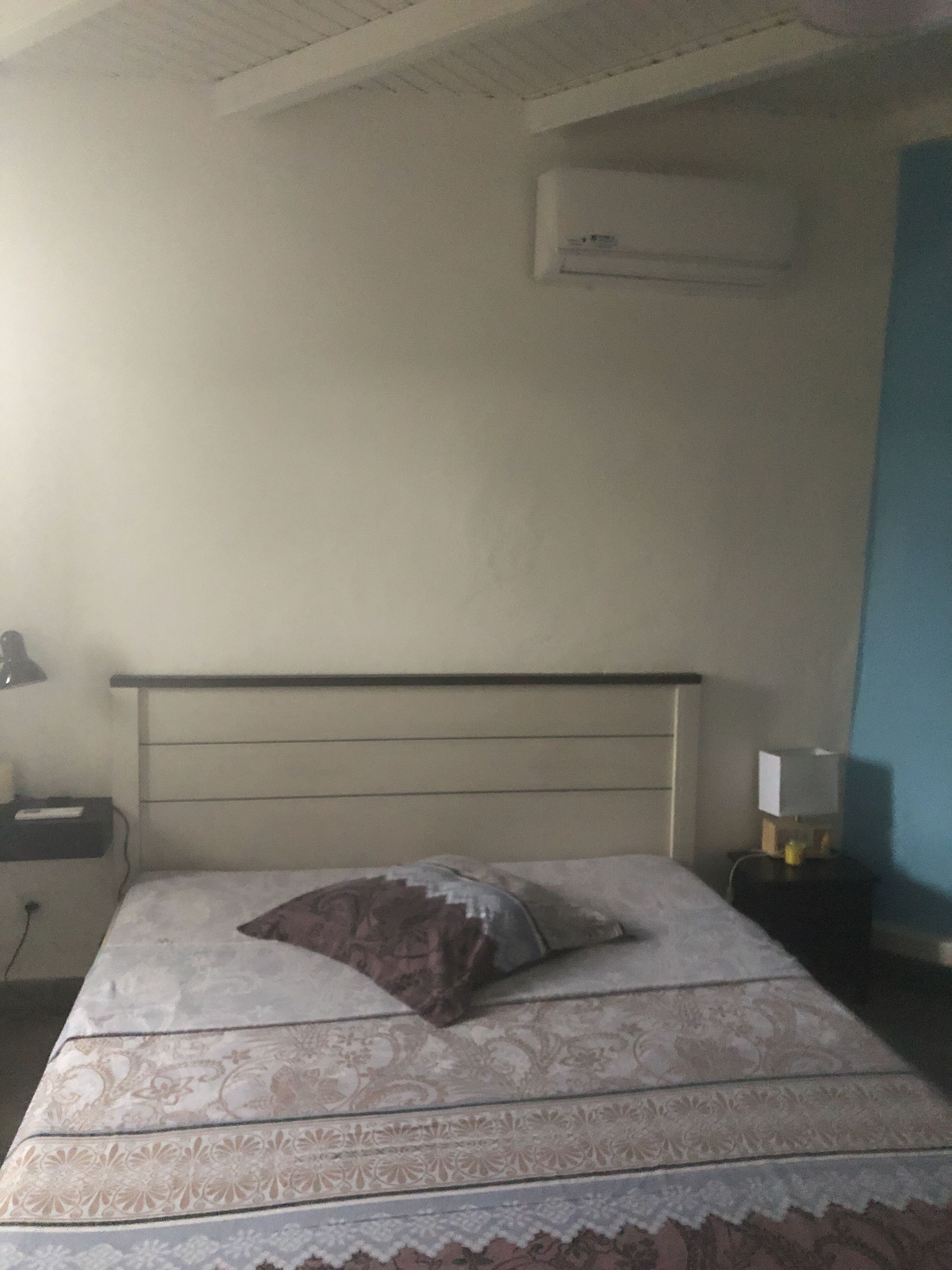 A bedroom with a bed, a nightstand, a lamp, and an air conditioning unit on the wall.