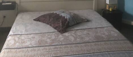 A bedroom with a bed, a nightstand, a lamp, and an air conditioning unit on the wall.