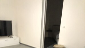 Ein modernes Wohnzimmer mit einem dunklen Sofa, einem Glastisch und einem Fernseher auf einer weißen Kommode.