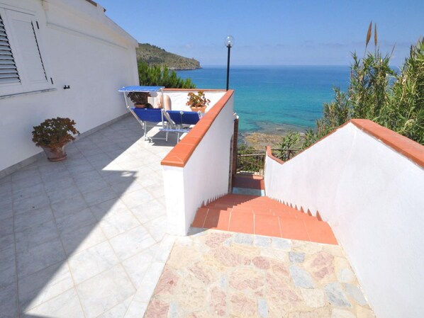 A staircase leading to a terrace with a view of the sea, a white building, and a blue sunshade.