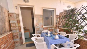 A patio area with a table set for two, white plastic chairs, a blue tablecloth, and a basket of bread. - Residence a Palinuro ID 558 (Palinuro)