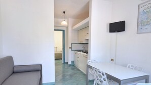 A compact living space with a kitchenette, a dining area with white chairs, and a gray sofa. - Residence a Palinuro ID 558 (Palinuro)