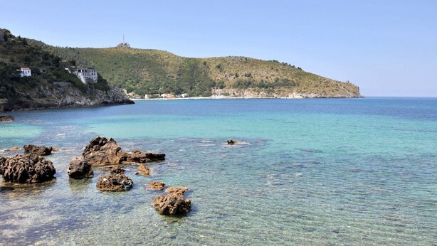 A coastal landscape with clear water, rocky shore, and a hill with buildings. - Residence a Palinuro ID 558 (Palinuro)