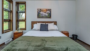 A bedroom with a large bed, two nightstands, a wooden headboard, a green blanket, and a painting of animals on the wall. - Lake + Ledge Retreat l Modern Luxury Home on Pike Lake (Hatley)