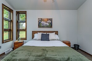 A bedroom with a large bed, two nightstands, a wooden headboard, a green blanket, and a painting of animals on the wall. - Lake + Ledge Retreat l Modern Luxury Home on Pike Lake (Hatley)