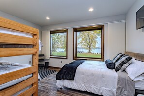 A bedroom with a bunk bed, a large bed with a view of a lake, and a window with a view of trees. - Lake + Ledge Retreat l Modern Luxury Home on Pike Lake (Hatley)
