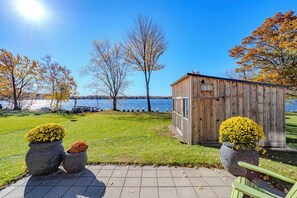 A wooden shed with a metal door, surrounded by grass and trees, near a body of water. - Lake + Ledge Retreat l Modern Luxury Home on Pike Lake (Hatley)