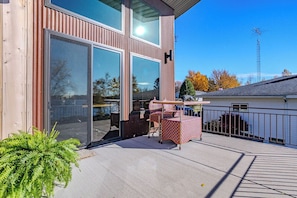 A modern building with large sliding glass doors, a covered outdoor seating area with a table and chairs, and a view of a body of water. - Lake + Ledge Retreat l Modern Luxury Home on Pike Lake (Hatley)