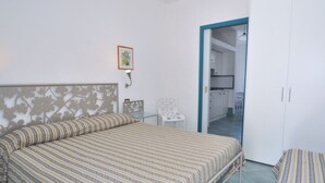 A bedroom with a bed, a chair, a small table, and a wardrobe.