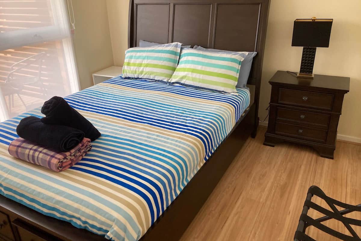 A neatly made bed with striped bedding, a dark wooden headboard, and a bedside table with a lamp.