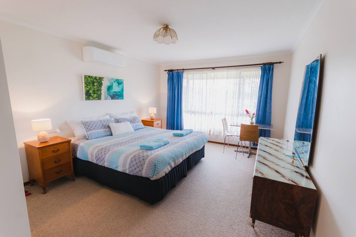 A bedroom with a bed, bedside tables, a desk, a chair, and a mirror.