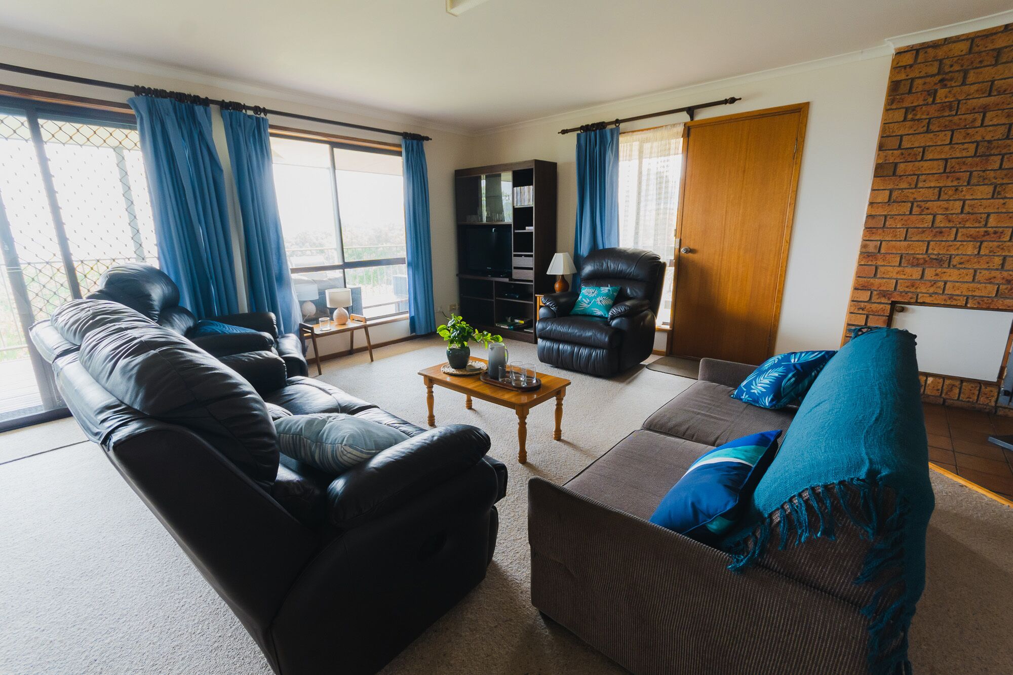 A living room with a leather sofa, a brown sofa, a coffee table, a black leather armchair, and a TV stand.