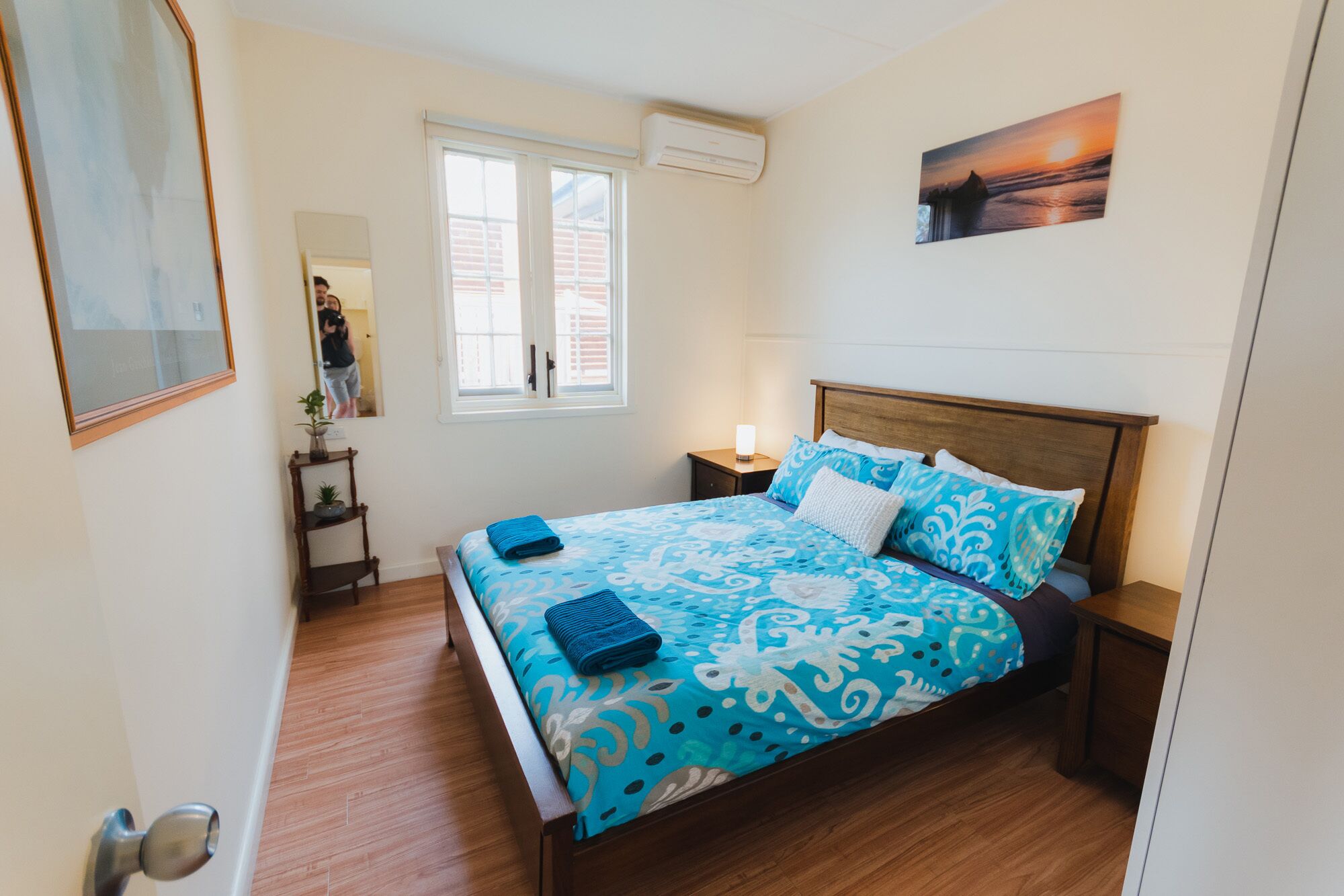 Un dormitorio con cama, mesita de noche, espejo, ventana y aire acondicionado.