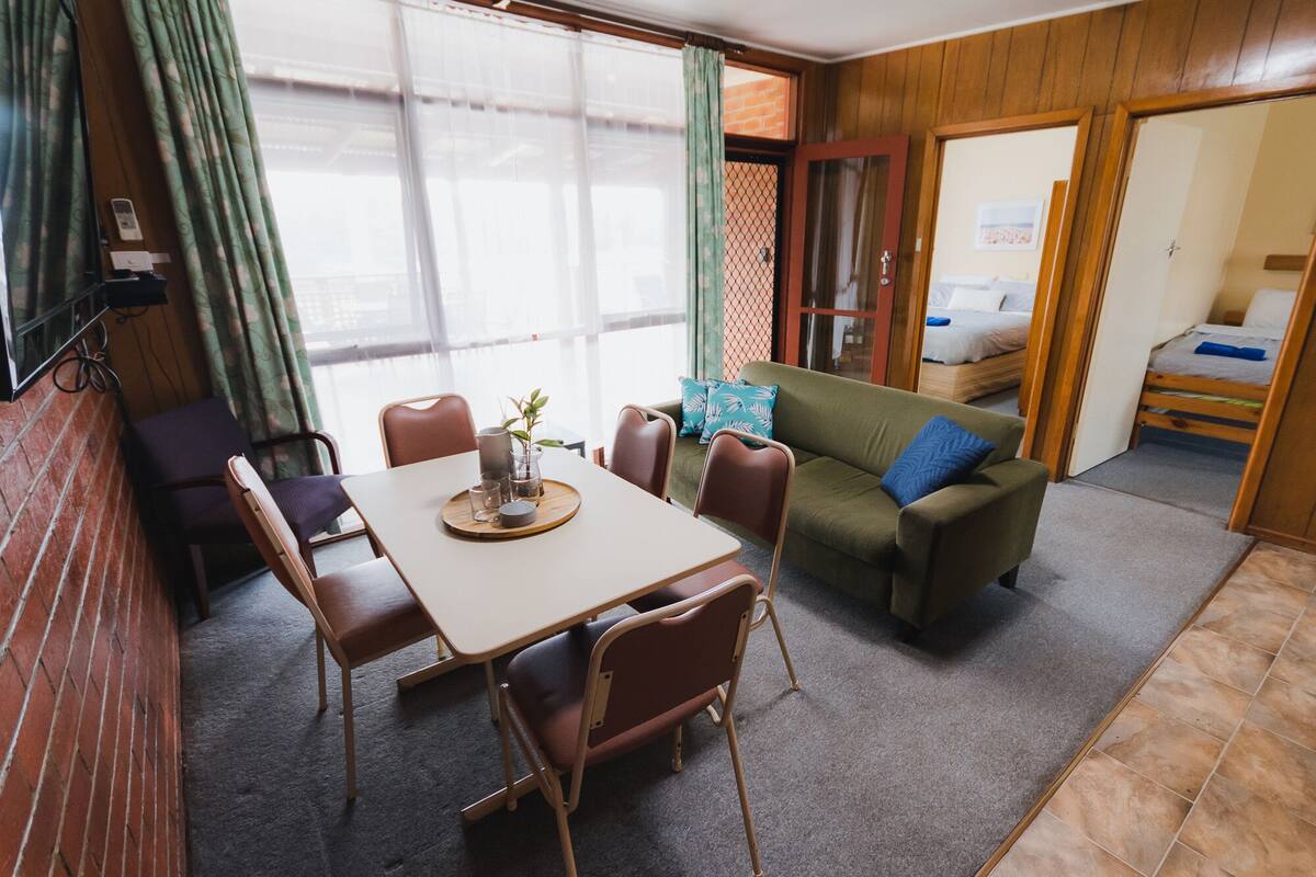 A compact living space with a dining table, chairs, a sofa, and a bunk bed.