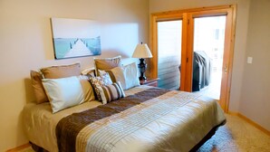 Una cama bien hecha con una colcha estampada, una lámpara de noche y vistas al exterior a través de una puerta.