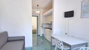 Ein kompakter Wohnraum mit Küchenzeile, einem Essbereich mit weißen Stühlen und einem grauen Sofa.