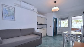 Ein gemütlicher Wohnbereich mit einer Couch, einem Esstisch und Stühlen. Im Hintergrund ist eine Küchenzeile erkennbar.