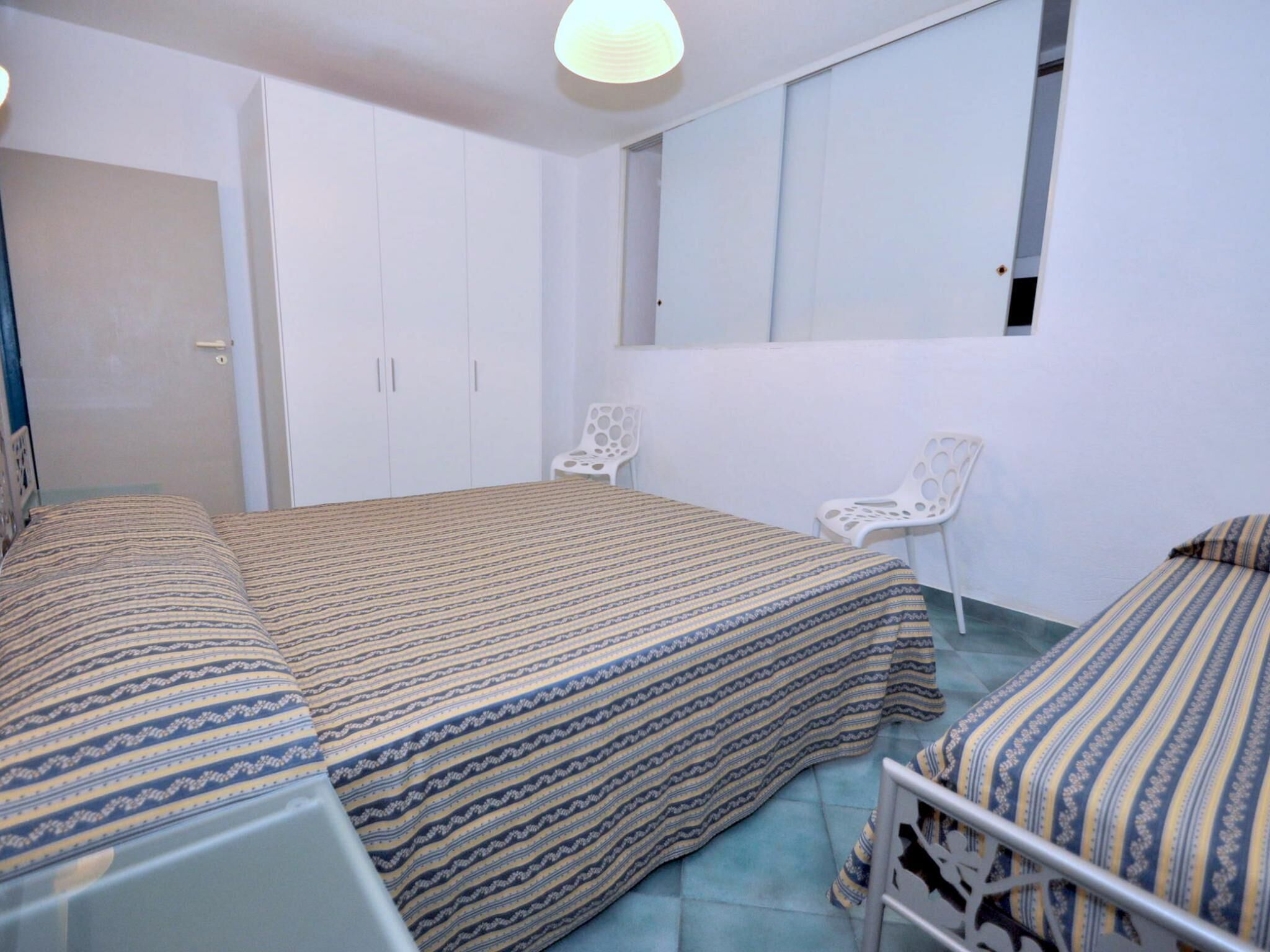 Ein Schlafzimmer mit zwei Betten, einem weißen Schrank, einem Sessel und einem Fenster.