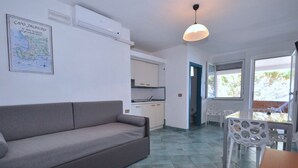 A compact living space with a sofa, dining table, and chairs, a kitchenette, and a map on the wall. - Residence a Palinuro ID 126 (Palinuro)