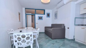A compact living space with a dining table and chairs, a sofa, and a kitchenette. - Residence a Palinuro ID 126 (Palinuro)