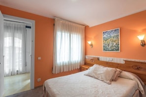 A bedroom with a bed, a window with curtains, a painting on the wall, and a nightstand.