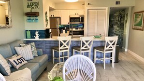 A modern living room with a grey sofa, white chairs, and a dining area with a white table. - Key Largo-Islamorada area-1 BR, 1 Bath -Privately Owned Condo -Fab Reviews! (Tavernier)