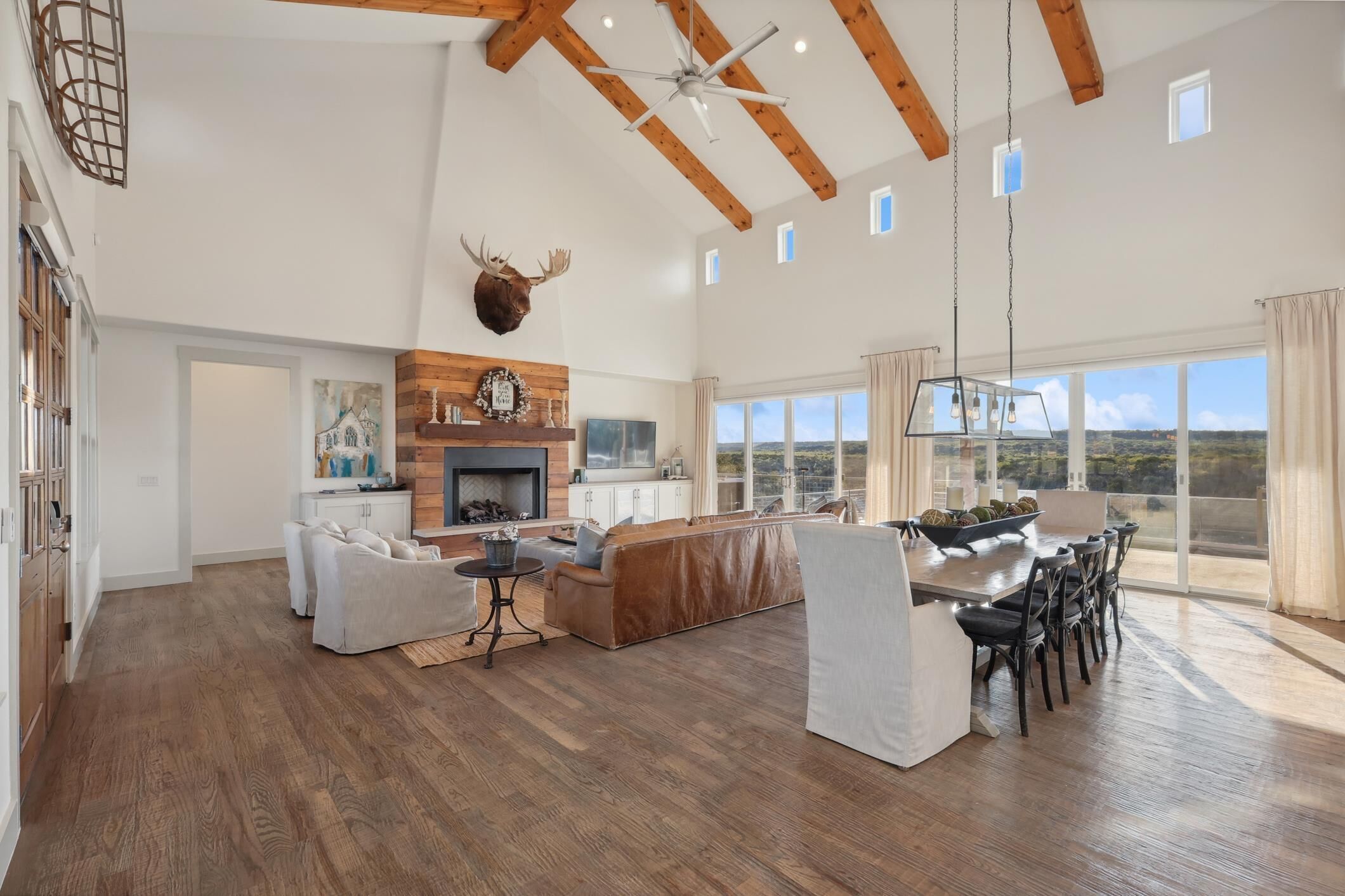 Amplia sala de estar con chimenea, vigas de madera, un ventanal con vistas y un comedor con mesa y sillas.
