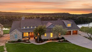 A two-story house with a stone facade, a large front porch, and a driveway leading to a garage. - PK LakeTime: 6 Bedroom/ 4 Bath Home with Dock, pool/hot tub, and game room (Strawn)