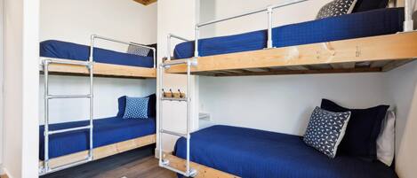 Un dormitorio con dos literas, cada una con una escalera metálica, y un pequeño estante blanco.