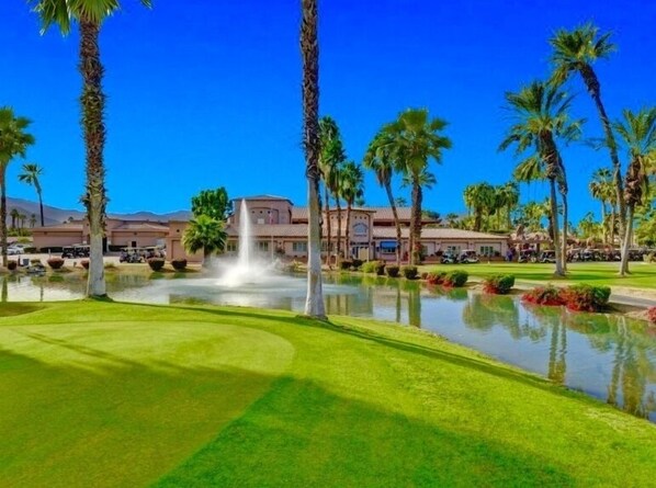 A golf course with a fountain, palm trees, and a building in the background.