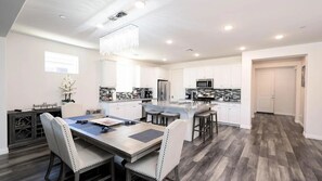 A modern kitchen with white cabinets, a central island, and a dining area with a table and chairs.