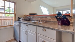 A kitchen with a dishwasher, sink, and a knife block on the countertop. - Very clean house with amazing park across the street and Japanese garden. (Coos Bay)