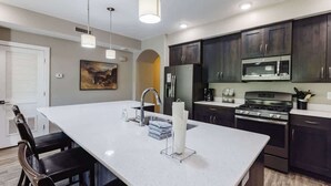 A modern kitchen with dark cabinets, a white countertop, stainless steel appliances, and pendant lighting.