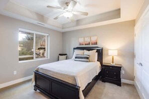 Une chambre à coucher comprenant un lit, une table de chevet, un ventilateur de plafond, une fenêtre et des œuvres d’art accrochées au mur.