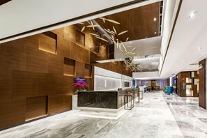 A modern lobby with a reception desk, wooden panel walls, and a marble floor.