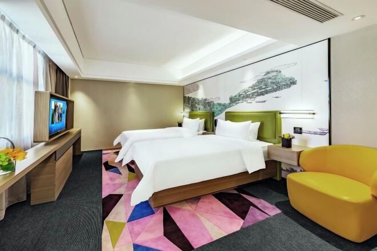 A hotel room with two beds, a TV, a desk, a chair, and a colorful rug.